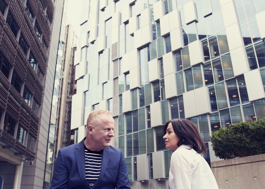 man and woman sitting on wooden bench outside buildings